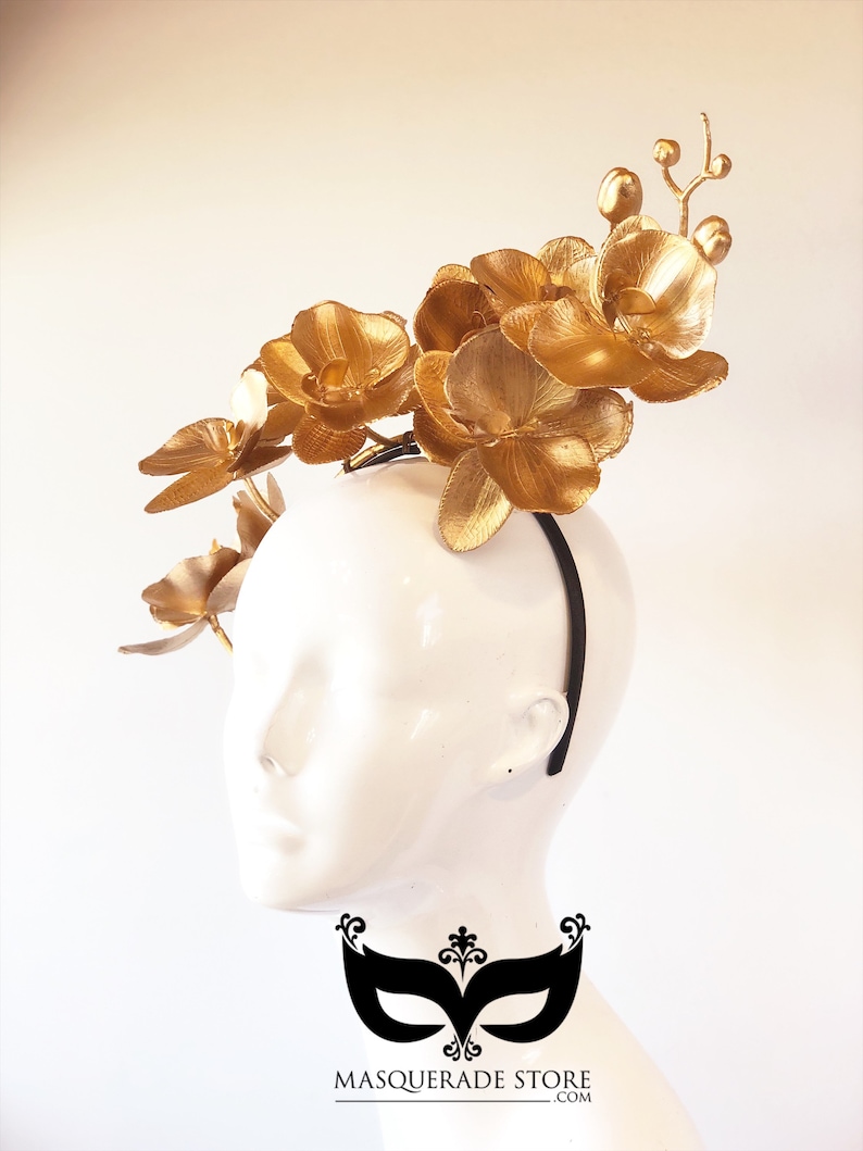 May include: Gold orchid flower headband. The headband is black and the flowers are gold. The headband is worn on a white mannequin head.