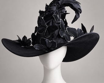 May include: A black pointed hat with a wide brim, featuring multiple black butterfly embellishments attached to the crown and brim. The fabric of the hat has a gathered, textured appearance, and the top of the hat is slightly curved.