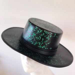 May include: A black fedora hat with a green floral design. The hat has a wide brim and a tall crown.