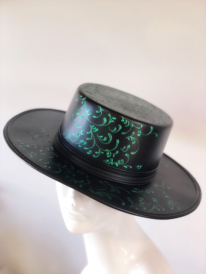 May include: A black fedora hat with a green floral design. The hat has a wide brim and a tall crown.