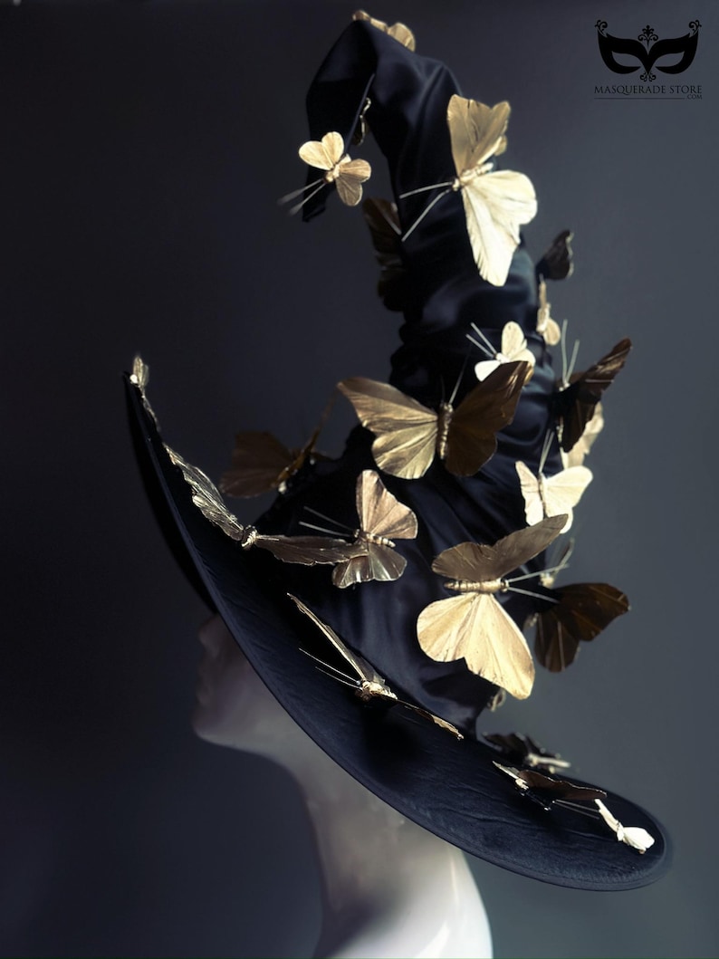 May include: A black witch hat adorned with numerous gold-colored butterfly embellishments. The hat has a wide brim and a tall, pointed crown. The text "MASQUERADE STORE" is visible on the upper right corner.