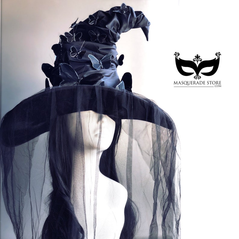 May include: A black witch hat with a tall, pointed crown adorned with blue butterfly embellishments. The hat is worn on a mannequin with long black hair and a black veil.