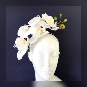 May include: A white headband with a cluster of white orchid flowers. The headband is worn on a white mannequin head.
