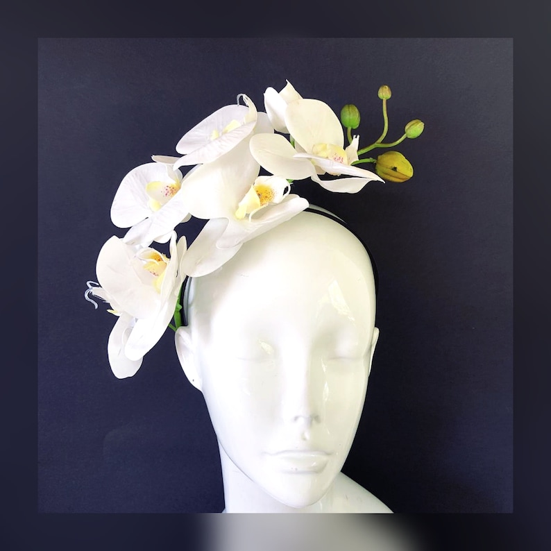 May include: A white headband with a cluster of white orchid flowers. The headband is worn on a white mannequin head.