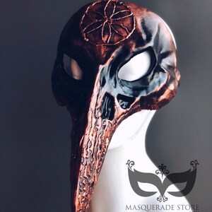 Pu&ograve; includere: Una maschera per il ballo in maschera personalizzata, di colore nero e rame, con un naso lungo e appuntito e un design circolare sulla fronte. La maschera &egrave; realizzata in un materiale strutturato e ha un design a forma di teschio.