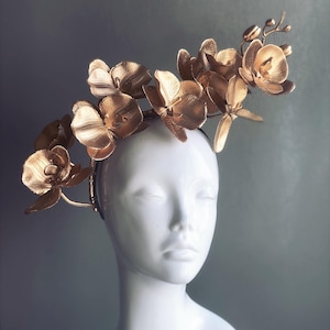 May include: A gold headband with a cluster of gold orchid flowers. The headband is worn on a white mannequin head.