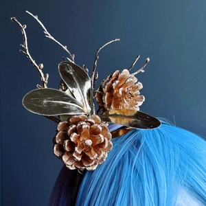 May include: Gold-toned pine cone and leaf hair comb with a twig design. The comb is on a blue wig.