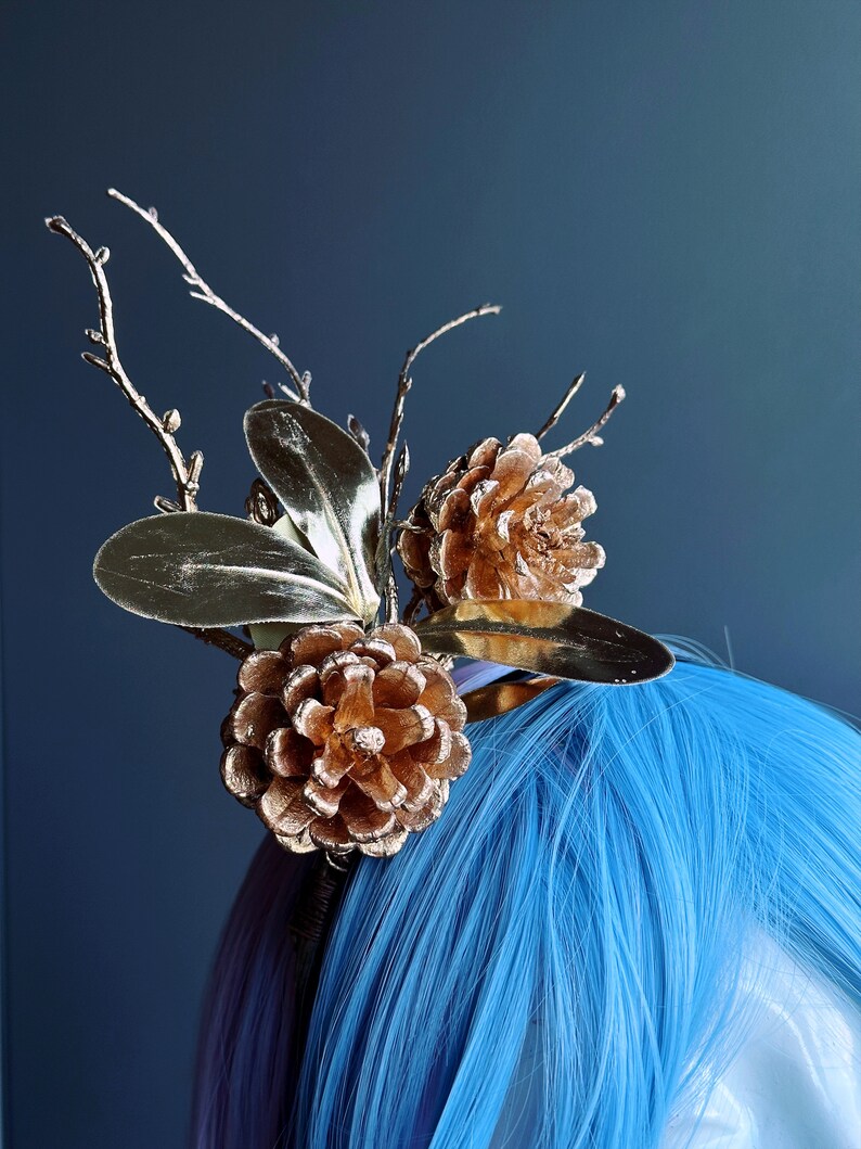 May include: Gold-toned pine cone and leaf hair comb with a twig design. The comb is on a blue wig.