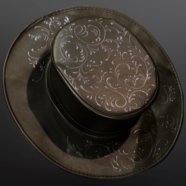 May include: A dark brown top hat with a wide brim and a cylindrical crown. The hat features an intricate silver floral pattern across the crown and brim, creating a decorative design. The hat is likely made of a leather-like material.