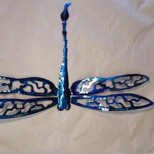 May include: A blue metal dragonfly wall decor with intricate cutouts in the wings. The dragonfly is mounted on a white background.
