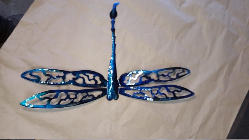 May include: A blue metal dragonfly wall decor with intricate cutouts in the wings. The dragonfly is mounted on a white background.