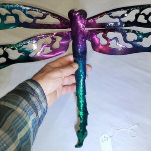 May include: A metal dragonfly wall art with a green, purple, and blue ombre finish. The dragonfly has intricate cutouts in its wings.