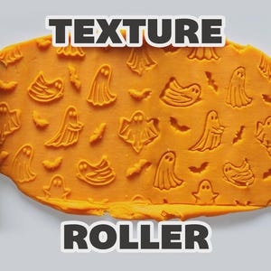 May include: Two light green cylindrical texture rollers flanking a flat sheet of orange dough. The dough is embossed with a repeating pattern of small ghosts and bats. The text "TEXTURE ROLLER" is displayed in bold white letters at the top and bottom.