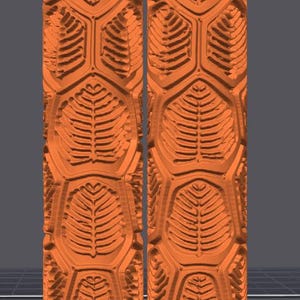 May include: Two identical orange cylindrical rollers featuring a repeating embossed pattern of stylized fern leaves arranged within a hexagonal grid structure. The surface texture is deeply carved with raised leaf veins and geometric borders.