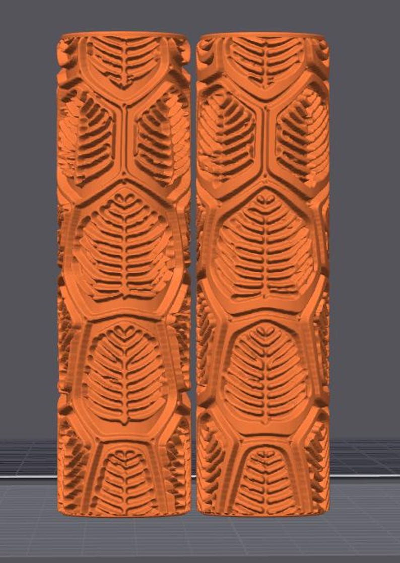 May include: Two identical orange cylindrical rollers featuring a repeating embossed pattern of stylized fern leaves arranged within a hexagonal grid structure. The surface texture is deeply carved with raised leaf veins and geometric borders.