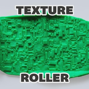 May include: A white cylindrical texture roller with a complex geometric pattern, shown alongside a green clay impression displaying the same intricate, raised, blocky, and layered design. The text "TEXTURE ROLLER" is printed in bold white letters.