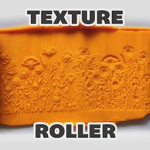 May include: Two light blue cylindrical texture rollers flanking a central orange slab of clay. The clay features an embossed pattern of various wildflowers and grasses. The text "TEXTURE ROLLER" is displayed in bold white letters at the top and bottom.