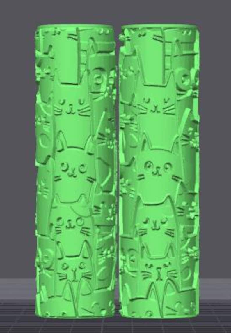 May include: Two cylindrical light green rollers featuring a repeating embossed pattern of various cat faces. The surface of each roller is covered in stylized feline features including ears, eyes, and whiskers, creating a continuous texture.