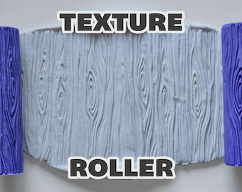 May include: Two purple cylindrical texture rollers with a wood grain pattern positioned on either side of a white clay slab that has been imprinted with the same wood grain texture. The text "TEXTURE ROLLER" is displayed in bold white letters.