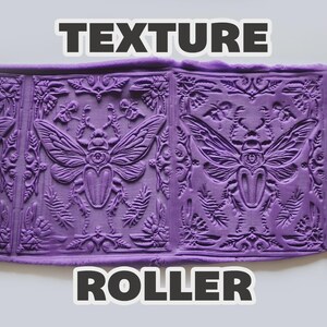 May include: An orange cylindrical texture roller with a repeating beetle and floral pattern, shown pressing into a flat sheet of purple clay. The text "TEXTURE ROLLER" is displayed in bold white letters at the top and bottom of the image.
