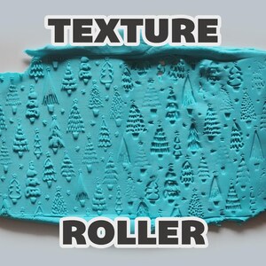 May include: Two pink cylindrical texture rollers with engraved Christmas tree patterns flanking a flat, rectangular piece of light blue modeling clay that has been imprinted with the same repeating forest of various evergreen tree designs.