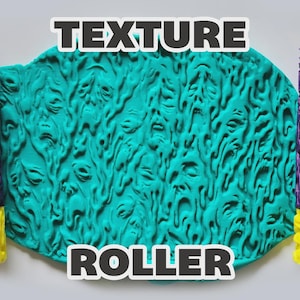 May include: Two cylindrical texture rollers with purple and yellow sections, featuring a relief pattern of multiple faces. Between the rollers is a teal slab of material embossed with the same face pattern. The text TEXTURE ROLLER is visible.