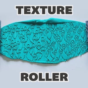 Può includere: Un rullo per texture cilindrico grigio con un motivo ripetuto di facce di anatra, mostrato accanto a una lastra di argilla color ottanio impressa con lo stesso disegno. Il testo "TEXTURE" appare in alto e "ROLLER" in basso.