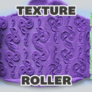 May include: Two light green cylindrical texture rollers flanking a central piece of purple clay. The clay is embossed with a repeating pattern of snakes. The text "TEXTURE ROLLER" is overlaid in white letters with a black outline at the top and bottom.
