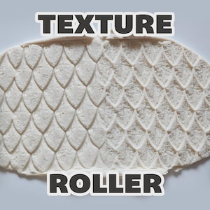 May include: A purple cylindrical texture roller with a dragon scale pattern, shown pressing into a flat piece of off-white clay to create a repeating embossed design. The image includes the text "TEXTURE ROLLER" in bold white letters.