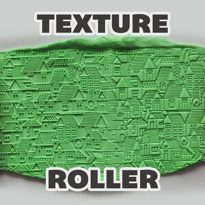 May include: A pink texture roller with a repeating house pattern, shown alongside a green clay slab imprinted with the same house design. The text "TEXTURE ROLLER" is displayed in white letters with a black outline at the top and bottom.