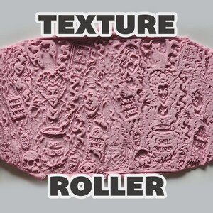 May include: A purple cylindrical texture roller positioned on either side of a pink clay slab. The clay features embossed designs of three witches, a cat, a skull, a pumpkin, and cauldrons with the text I SMELL CHILDREN and AMUCK AMUCK AMUCK.