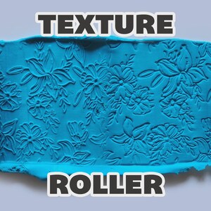 May include: A light orange cylindrical texture roller featuring an intricate floral pattern, shown alongside a strip of bright blue clay that has been embossed with the same floral design. The text "TEXTURE ROLLER" is displayed in bold white letters.