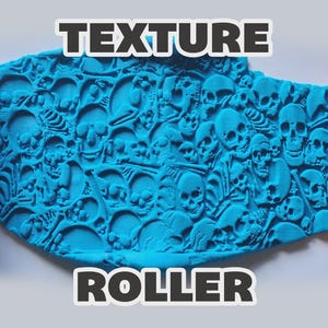 May include: An orange cylindrical texture roller with a repeating skull and bone pattern, shown pressing into a flat piece of bright blue clay. The text "TEXTURE ROLLER" is printed in bold white letters with a dark outline above and below the clay.