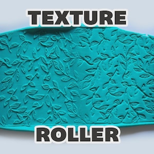 May include: A bright blue cylindrical texture roller featuring a detailed embossed leaf and vine pattern, shown alongside a teal clay slab that displays the same intricate botanical impression. The text TEXTURE ROLLER is visible.