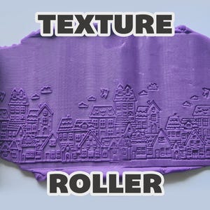 May include: A green cylindrical texture roller positioned on either side of a purple clay slab. The clay features an embossed pattern of a small town with houses, windows, doors, and clouds. The text "TEXTURE ROLLER" is displayed in white letters.