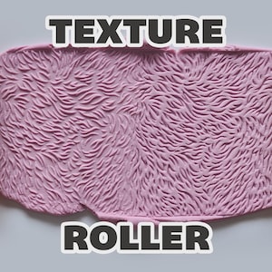 May include: An orange cylindrical texture roller with a raised fur-like pattern positioned on both sides of a light purple slab of material that has been imprinted with the same fur-like texture. The text "TEXTURE ROLLER" is visible.