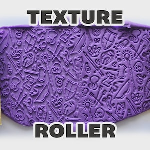 May include: Two yellow cylindrical texture rollers flanking a central purple sheet of clay. The rollers feature engraved fantasy motifs including swords, shields, skulls, bows, arrows, and treasure chests, which are imprinted into the purple clay surface.