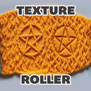 May include: A bright blue texture roller with a flame pattern, shown alongside a flattened piece of orange clay that has been imprinted with two pentagram symbols surrounded by a detailed flame texture. The text TEXTURE ROLLER is visible.