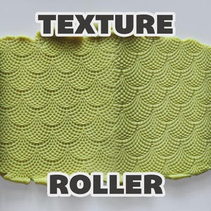 May include: A purple cylindrical texture roller with a repeating scale pattern, shown pressing into a flat piece of light green clay. The clay displays a deep, embossed impression of the same scale design. The text TEXTURE ROLLER is visible.