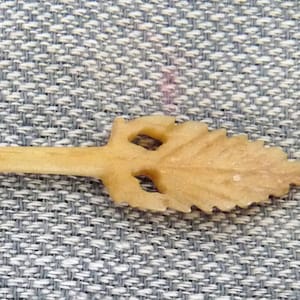 May include: A small, off-white, wooden spoon with a carved leaf design on the handle.