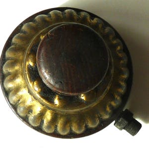 May include: A round, decorative knob with a dark wood center and a gold-colored outer ring. The outer ring has a rope-like design.