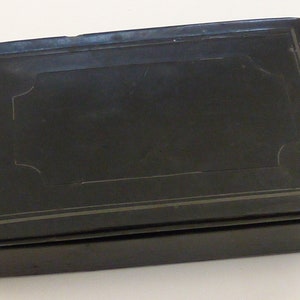 May include: A black rectangular box with a silver-colored border and a silver-colored design on the top. The box is closed.