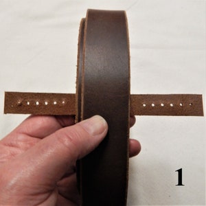 Shown here the steps for fitting a replacement belt loop strap keeper.  Shown in a hand.
1. Center strip on double thickness of belt, strap.