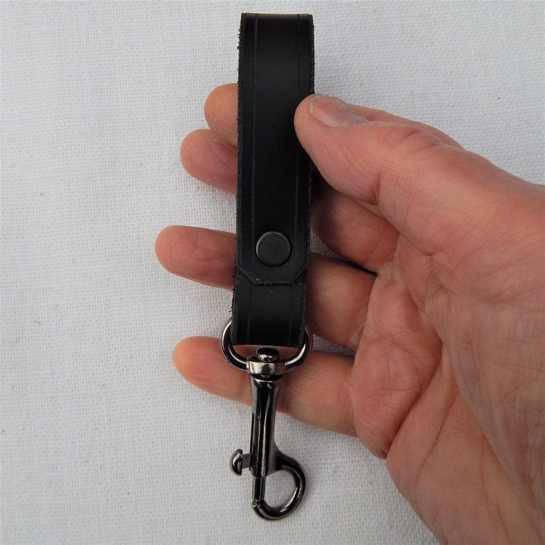 Simple, strong and useful leather loop with a metal spring clip firmly attached.  Use on a belt or strap to hold small items - such as keys, a hand towel, etc - or as a keyring in its own right.  Black shown in a hand