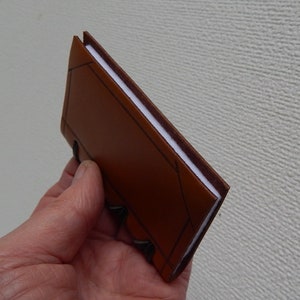 Neat Tan leather covered needle case with four white felt pages for your pins, needles etc. in a variety of different leathers and colours.  Decorated with incised lines to resemble a bound book with a thong stitched spine.  Showing side view
