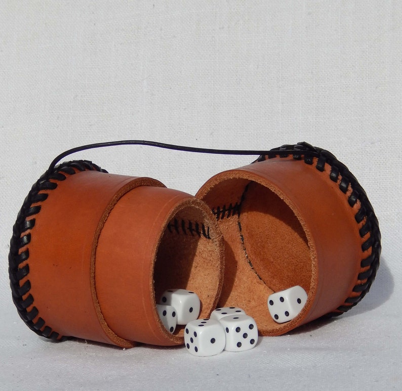 A circular leather pot open, lying down with snug fitting lid that can be used as a second pot.  Vegetable tanned leather with a plait like thonging around the base and top, shown here with dice, not included.