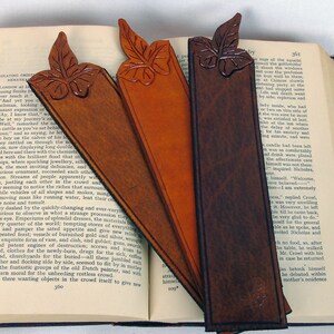 3 self colour, cut out leaf leather bookmarks  in different hues resting on an open book