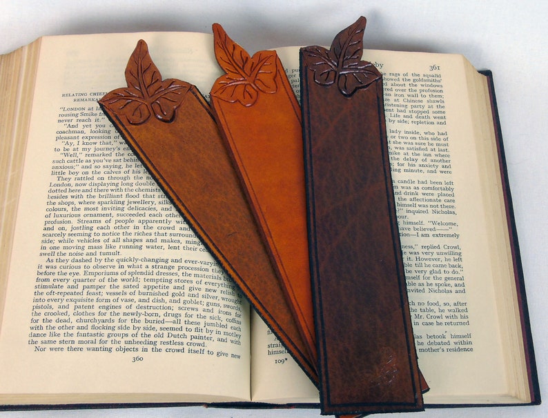 3 self colour, cut out leaf leather bookmarks  in different hues resting on an open book