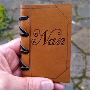 Neat leather covered needle case with four white felt pages for your pins, needles etc. in a variety of different leathers and colours.  Decorated with incised lines to resemble a bound book with a thong stitched spine.  Shown with personalisation