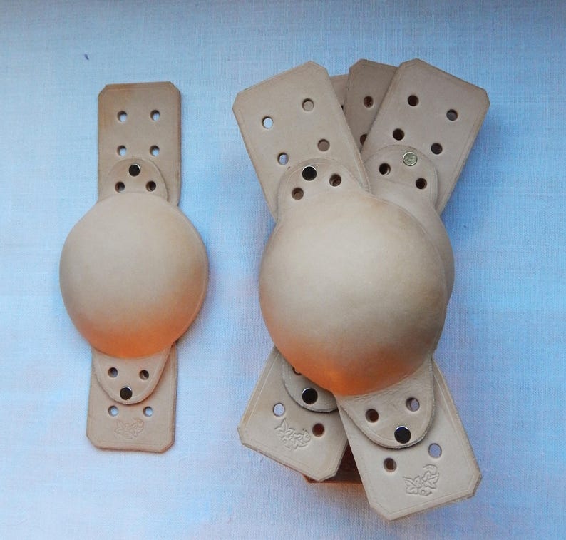 5 domed leather bell muffles in natural, vegetable tanned leather with overlays on a plain background.
5 fixing positions for ties.  All shown fitted with optional overlay to double thickness.  Handmade to fit most tower bells.